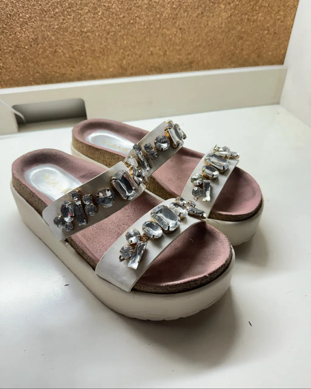 Sandalias blancas con dos tiras adornadas con piedras transparentes y plateadas. Suela plataforma blanca y plantilla rosa.