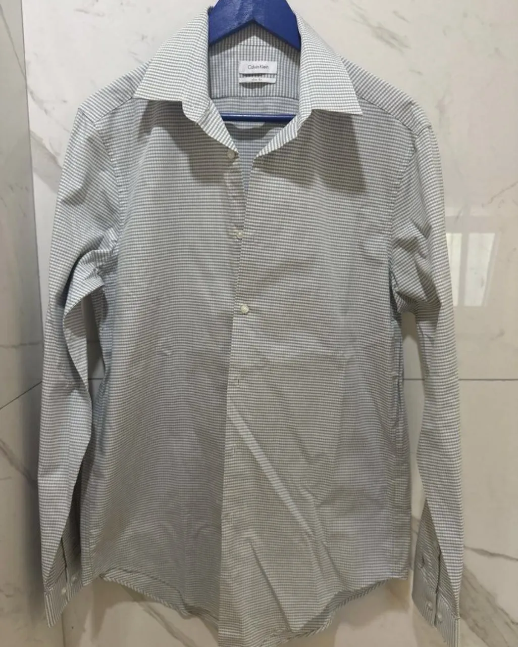 Camisa de vestir Calvin Klein, manga larga, con un sutil estampado a cuadros en tonos grises y blancos. Ideal para un look elegante y formal, perfecta para el trabajo o eventos especiales. Su corte slim fit asegura una silueta moderna y estilizada.