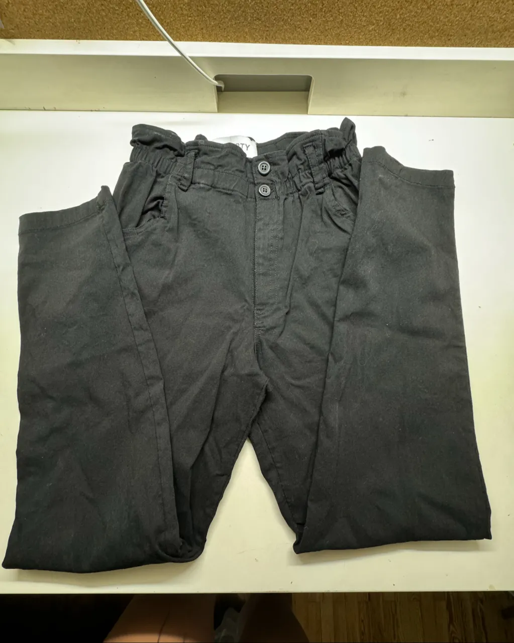 Pantalón negro con cintura elastizada y fruncida. Posee dos botones en la parte superior y bolsillos delanteros y traseros.