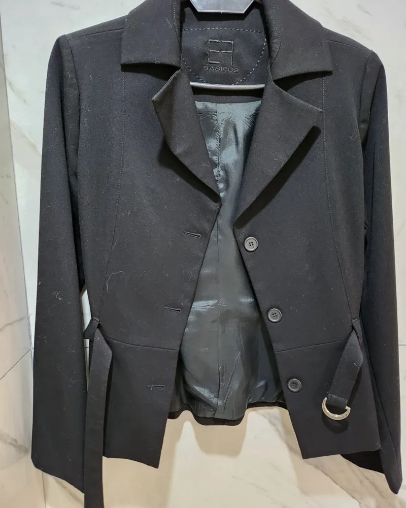 Blazer negro con cinturón y hebilla metálica. Posee botones al frente y solapas.