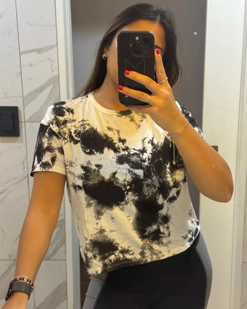 Remera blanca y negra con estampa tie-dye. Es corta y de mangas cortas, ideal para un look casual y moderno.