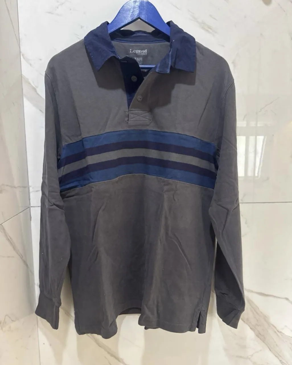 Remera manga larga de algodón gris con detalles a rayas azules en el pecho. Cuello polo con botones. Ideal para un look casual y cómodo.