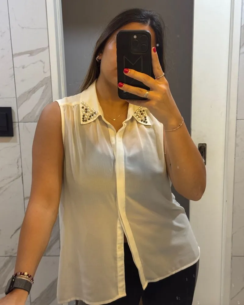 Camisa blanca sin mangas con cuello adornado con perlas y tachas. Un toque chic y moderno para cualquier ocasión.