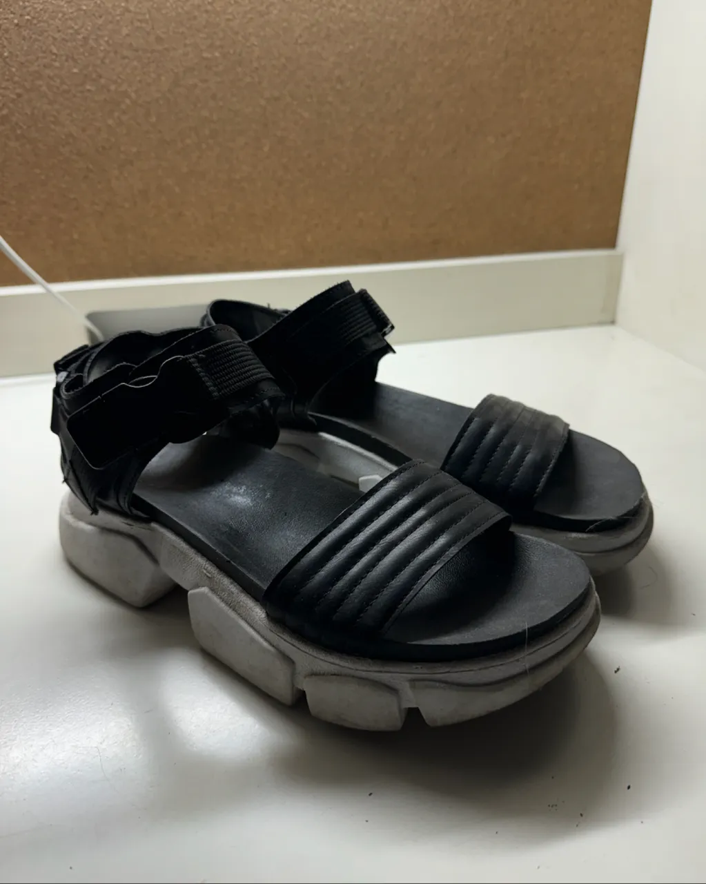 Sandalias negras con plataforma blanca. Tienen tiras anchas en el empeine y ajuste con hebilla en el tobillo.