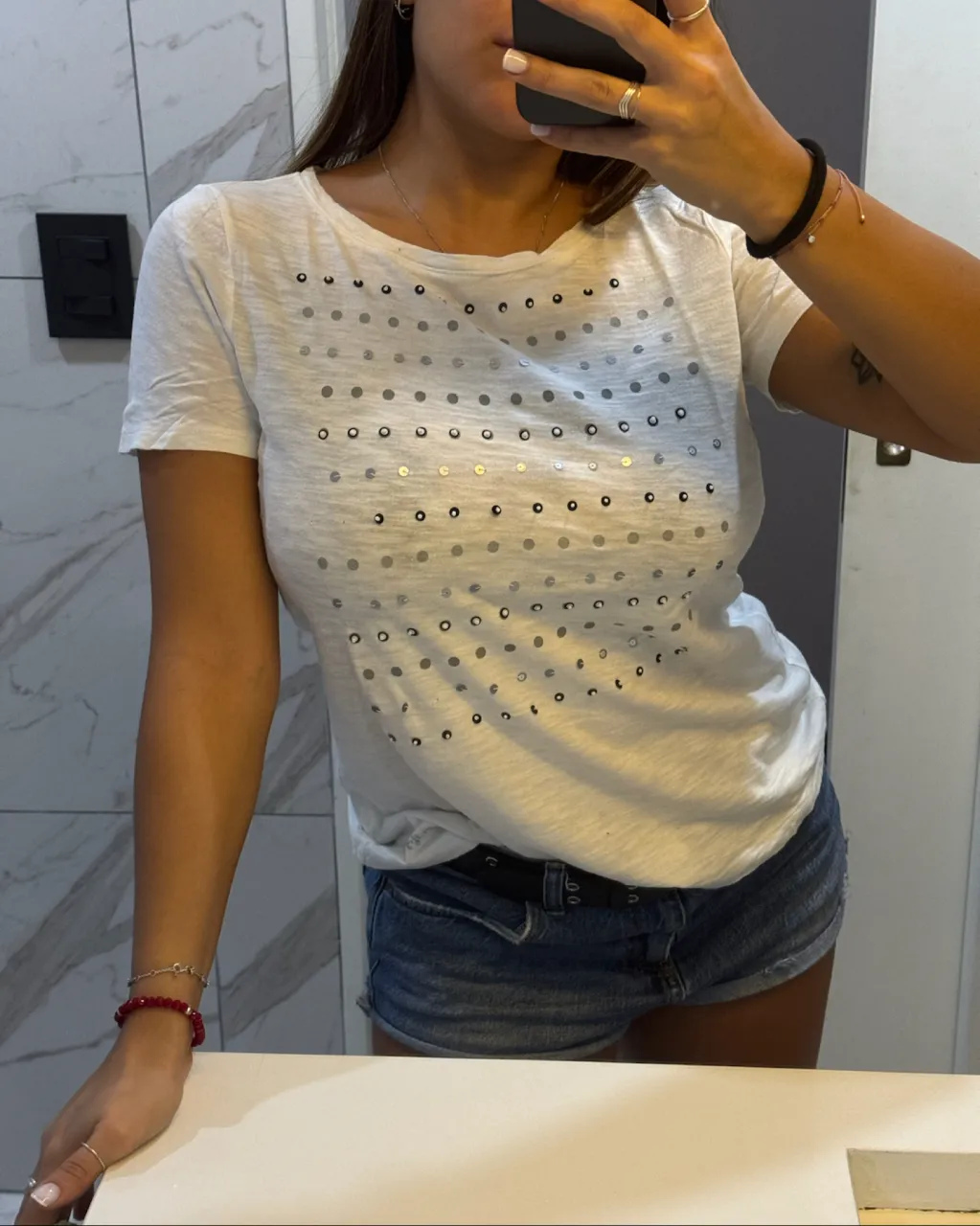 Remera blanca de manga corta con detalles de lentejuelas redondas plateadas y grises dispuestas en filas horizontales.