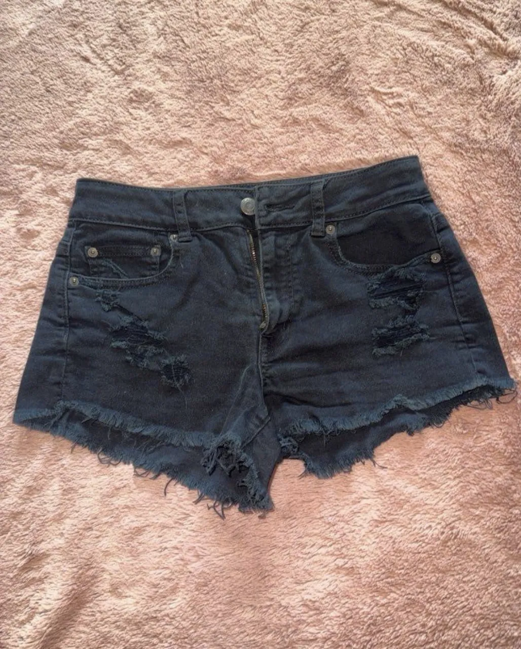 Shorts de jean negros tiro alto con roturas y detalles desflecados en los bordes. Un clásico para cualquier ocasión.