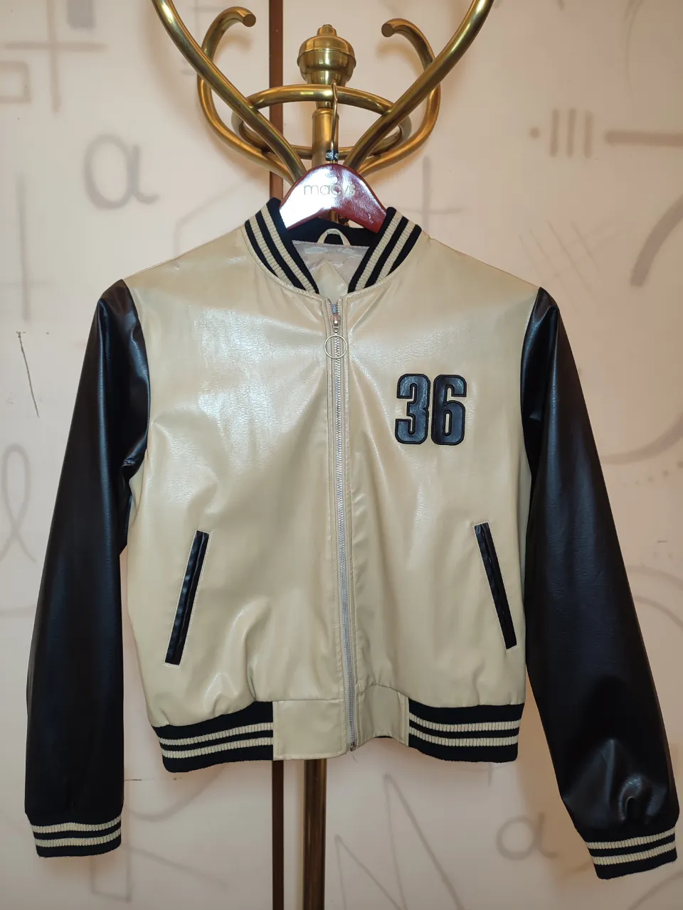 Campera estilo universitaria con mangas negras y cuerpo color crema. Posee un número 36 bordado en el frente. Tiene puños y cuello con franjas negras y blancas.Unisex