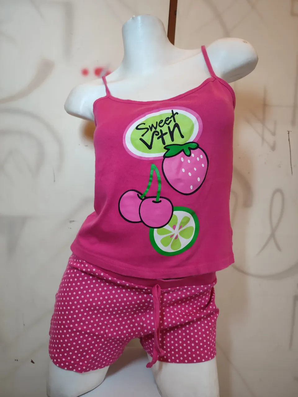 Conjunto de pijama de dos piezas. La remera es de breteles finos, color fucsia, con estampa de frutas (cerezas, fresa y rodaja de limón) y la frase "Sweet Vtn". El short es color fucsia con lunares blancos y cordón ajustable en la cintura.medidas en plano sin estirar musculosa sisa 40cm largo con bretel 47cm .Short cintura 42 cm,largo 24 cm 