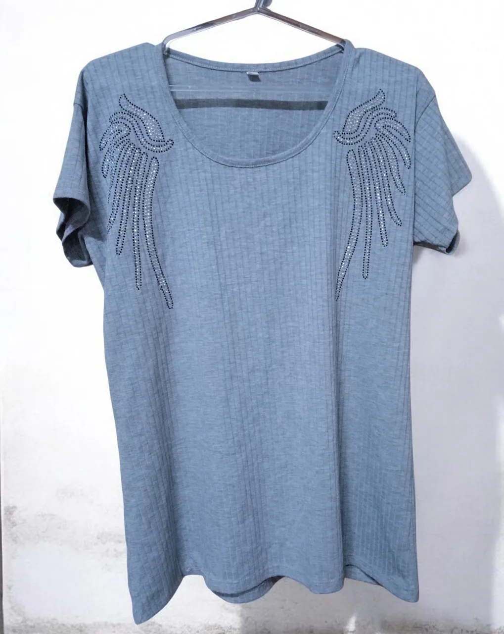 Remera gris de manga corta con cuello redondo. Posee un diseño de alas con strass en la zona de los hombros.