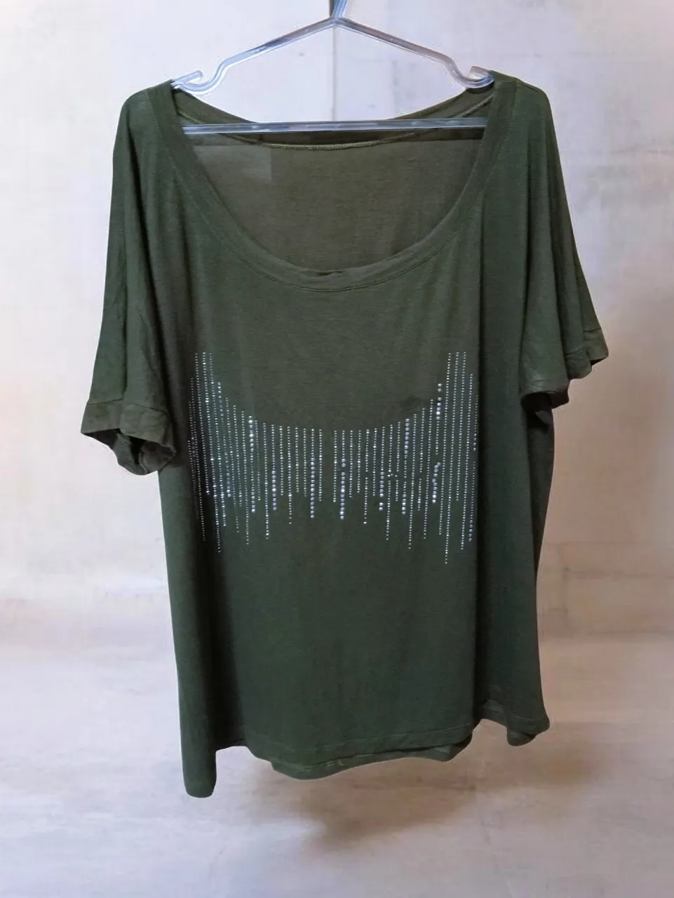 Remera de manga corta color verde. Posee un diseño de brillos plateados en la parte delantera que simula una curva con líneas verticales.