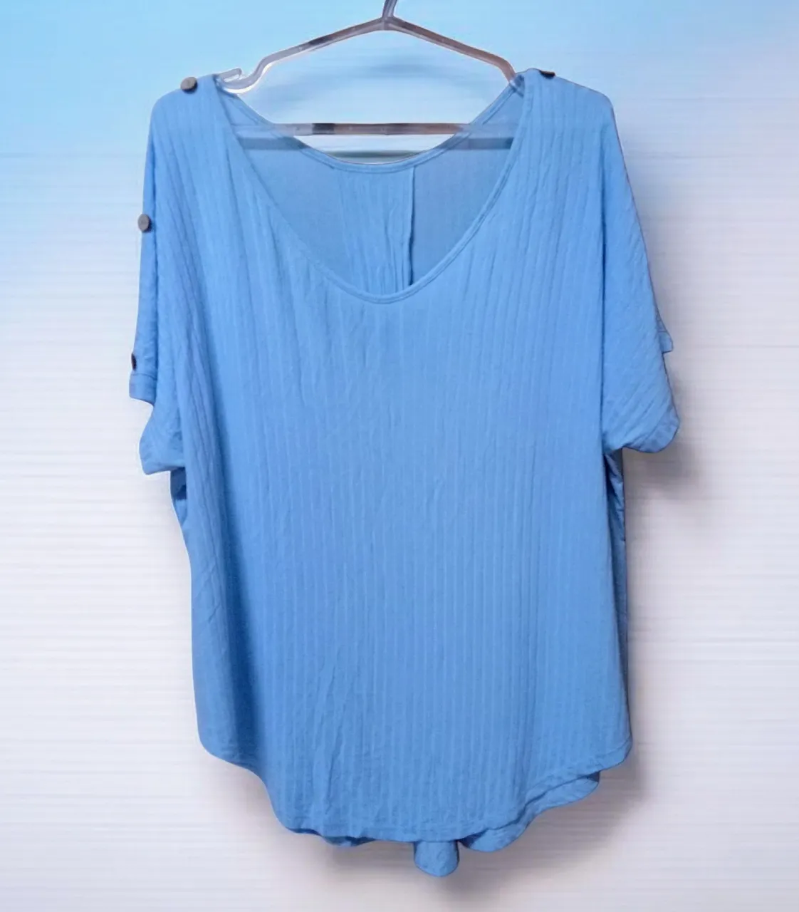 Remera azul de manga corta con cuello en V y detalle de botones en las mangas.