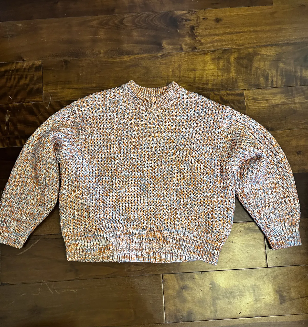 Sweater tejido con cuello redondo y mangas largas. Diseño multicolor con hilos en naranja, blanco y celeste.