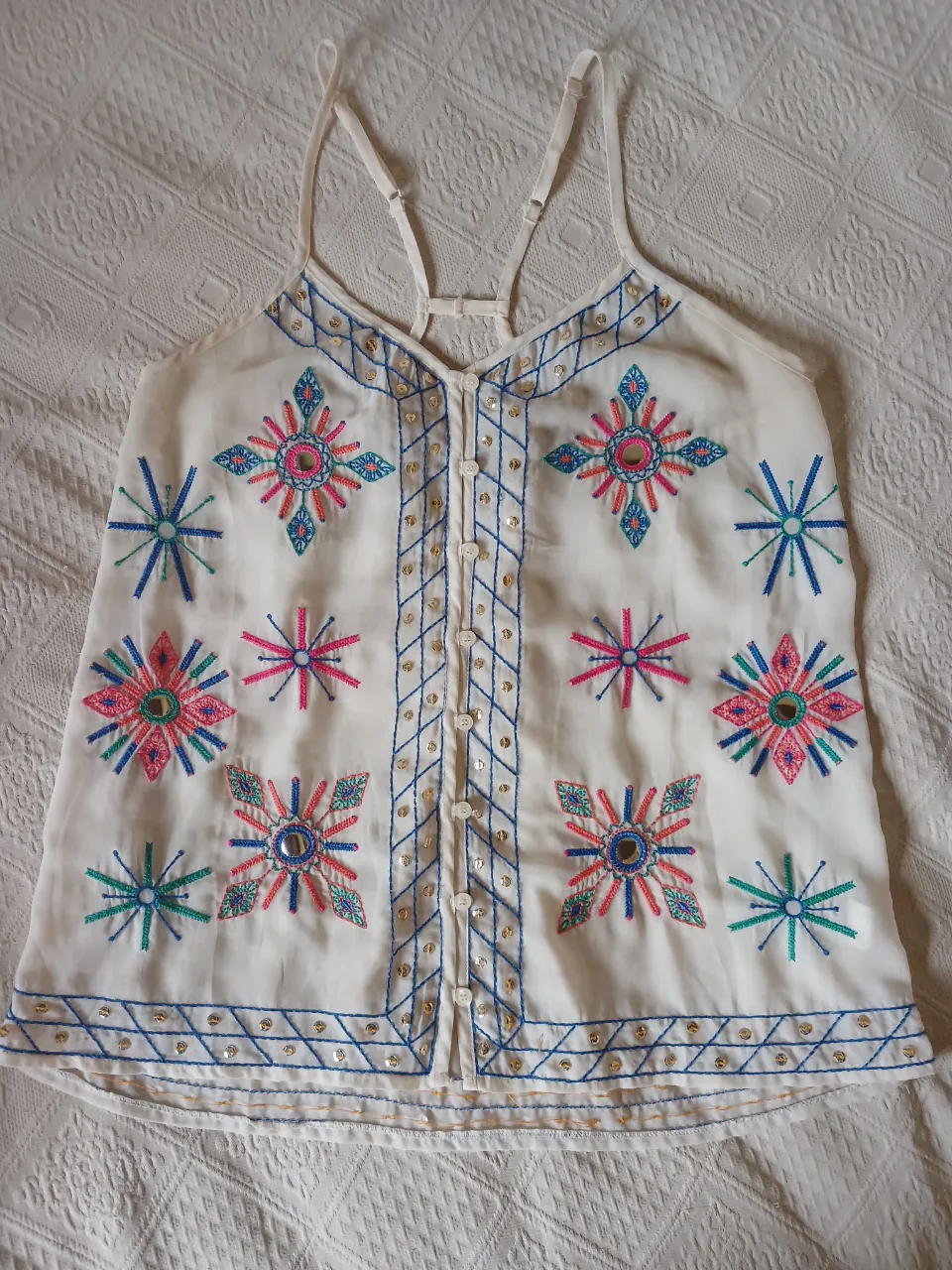 Musculosa blanca bordada en rosa, azul y verde. Con botones al frente. La foto del detalle es una lentejuela que le falta en la parte inferior, facil de colocar. 