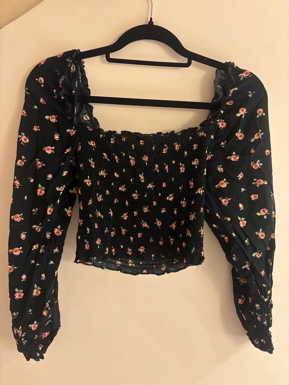 Top crop negro con estampa floral de flores rojas y rosas. Tiene mangas largas abullonadas y escote cuadrado con volados. El torso es fruncido y elastizado, lo que le da un calce perfecto. Ideal para un look canchero y femenino.