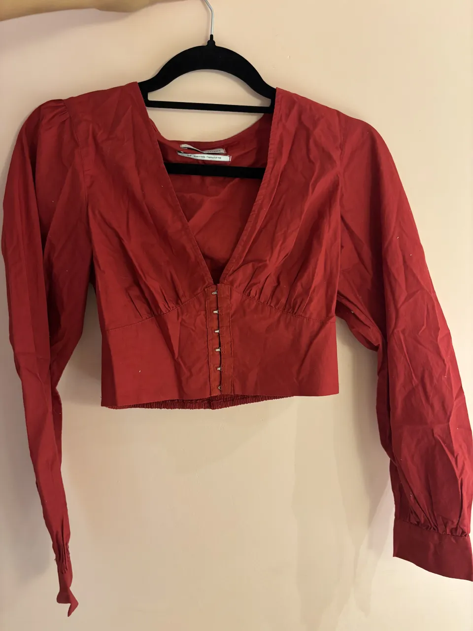 Blusa roja escotada con mangas largas abullonadas y detalle de ganchitos en el frente. Un modelo súper canchero y moderno, ideal para lucir en salidas nocturnas o eventos especiales. Su diseño crop la hace perfecta para combinar con jeans tiro alto o faldas.