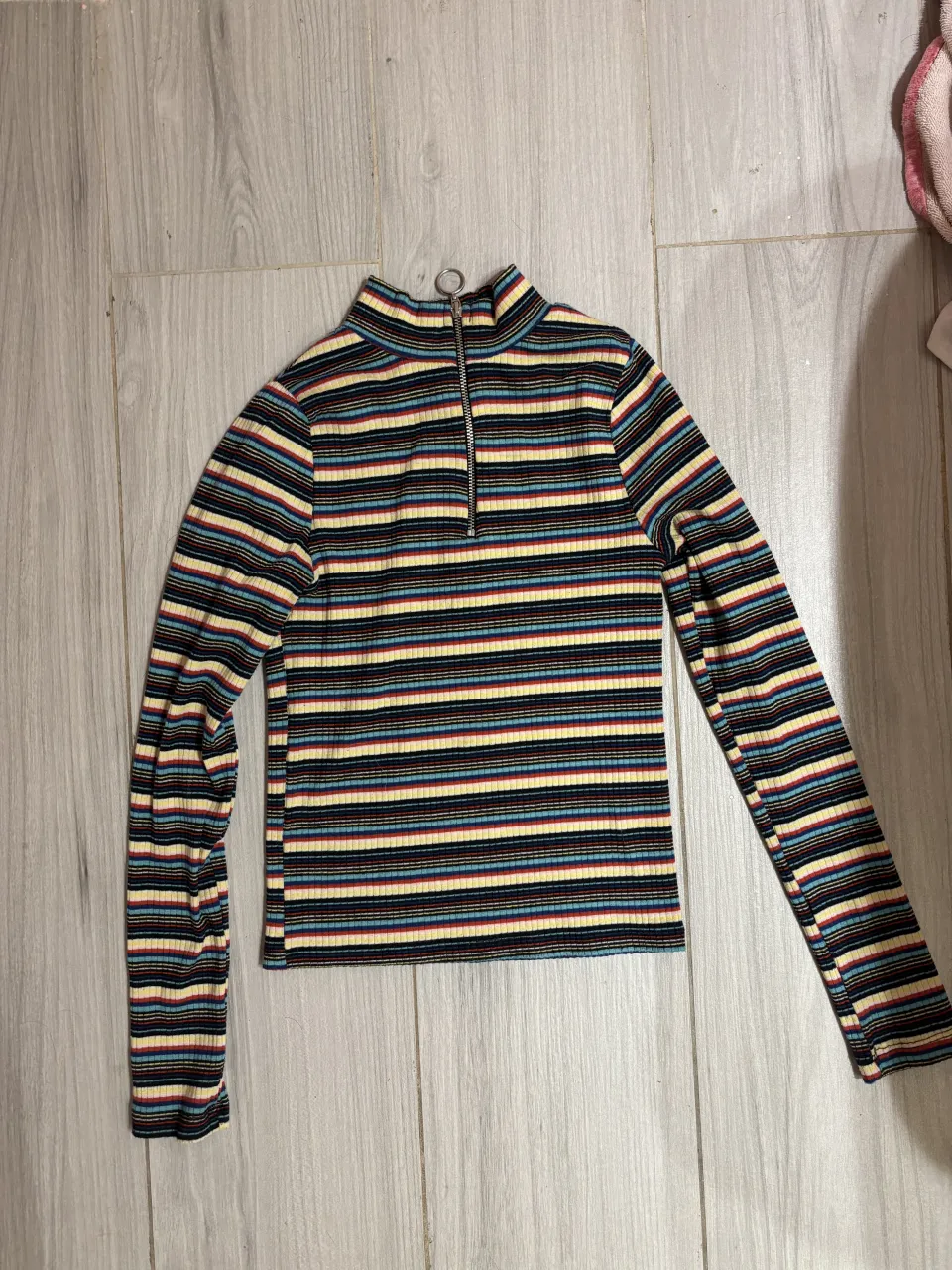 Remera manga larga a rayas multicolor con cuello alto y cierre metálico. Un básico canchero y versátil para tu día a día.