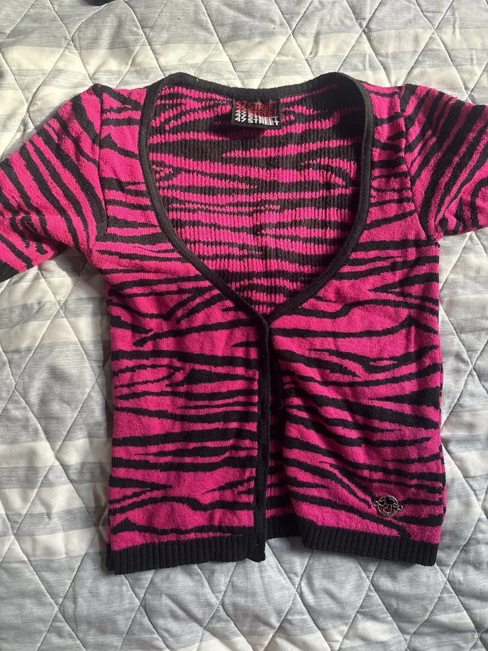 Cardigan súper canchero con estampa de cebra en fucsia y negro. Tiene botones al frente y un detalle metálico con corazones en la parte inferior. Ideal para darle un toque rocker a tu outfit.