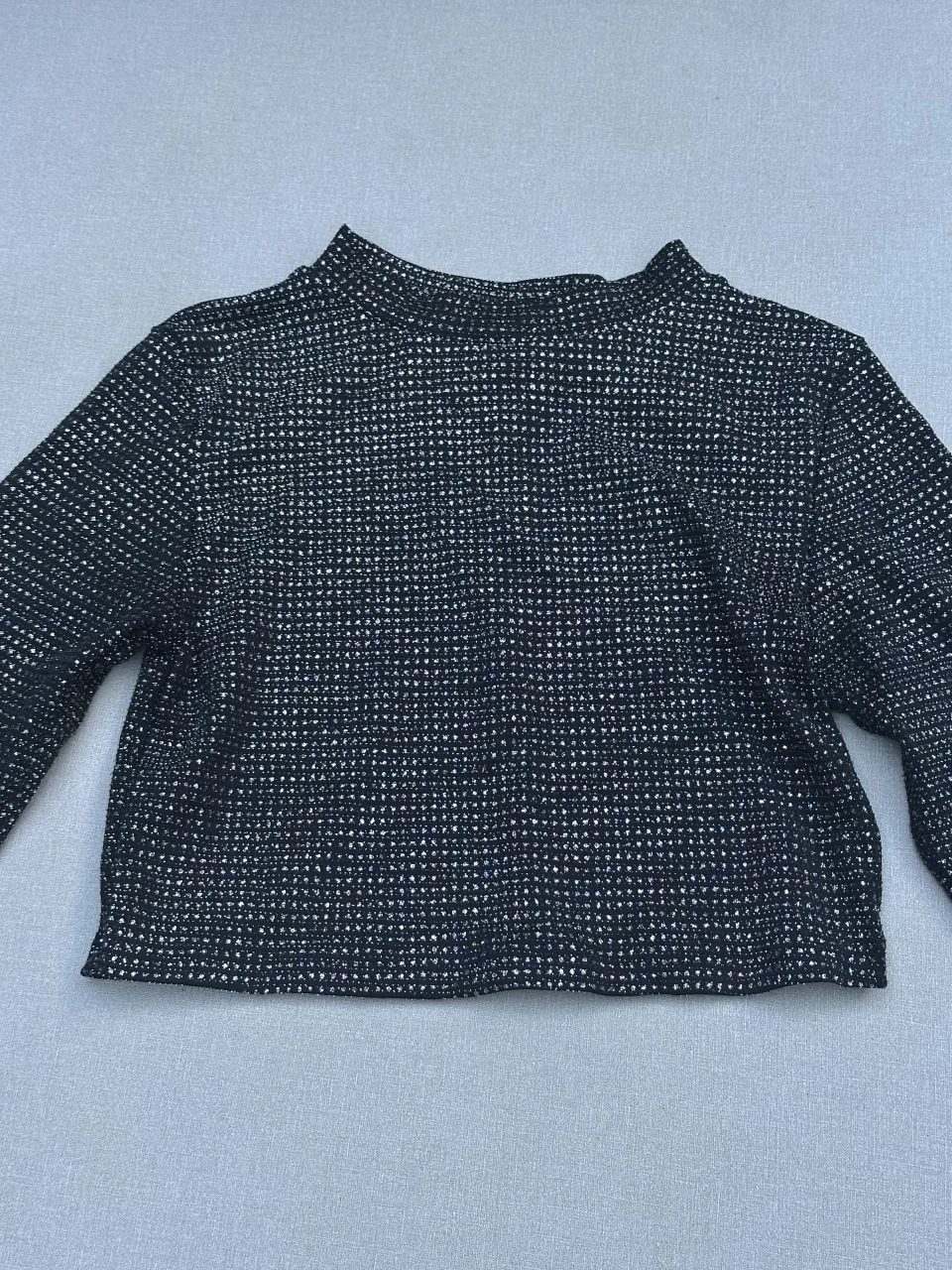 Remera manga larga con cuello alto y detalles plateados brillantes. Un diseño moderno y llamativo, perfecto para destacar en cualquier ocasión.