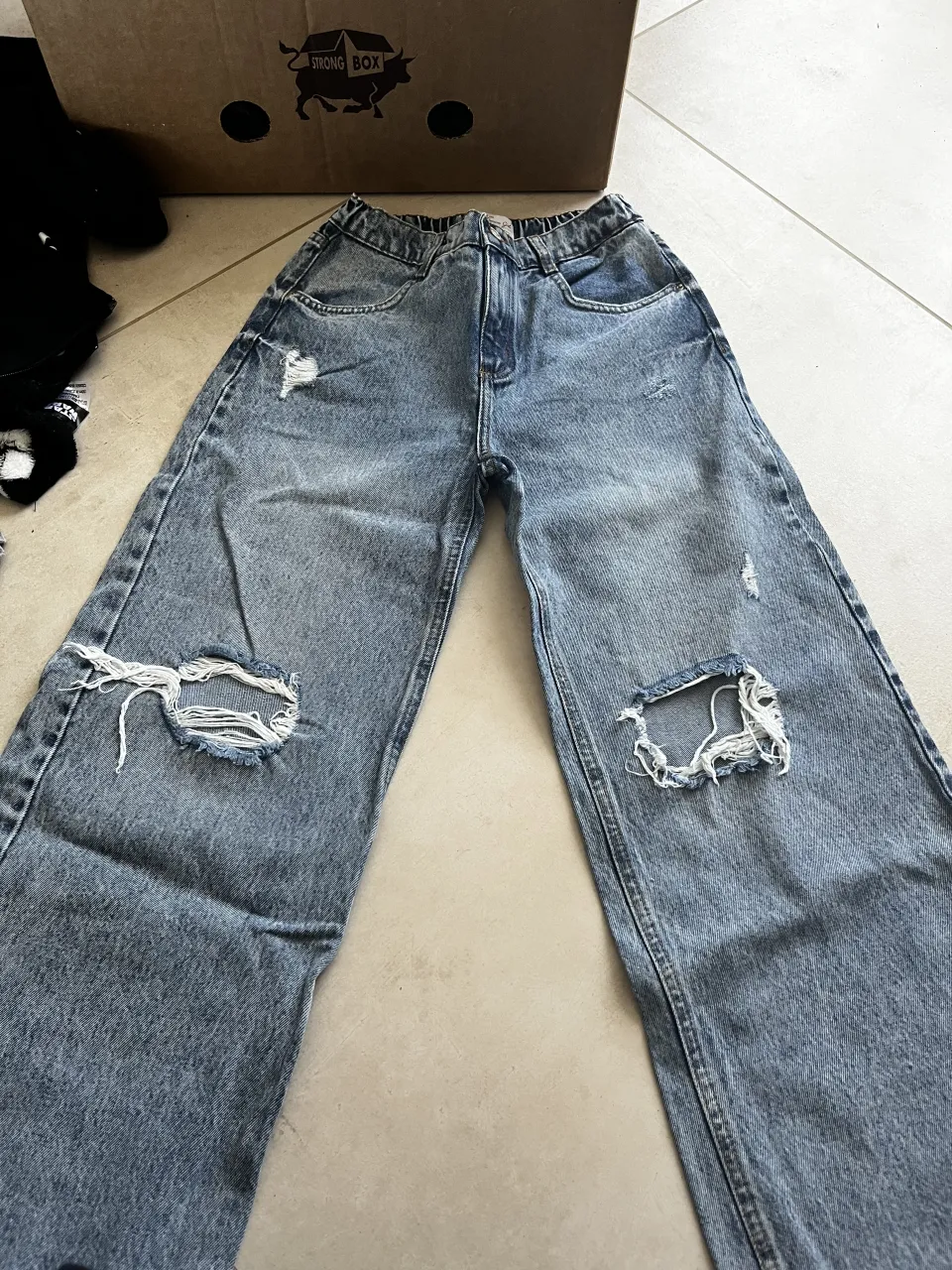 Jean de tiro alto con roturas en ambas rodillas y detalles desgastados. Cintura con elástico.