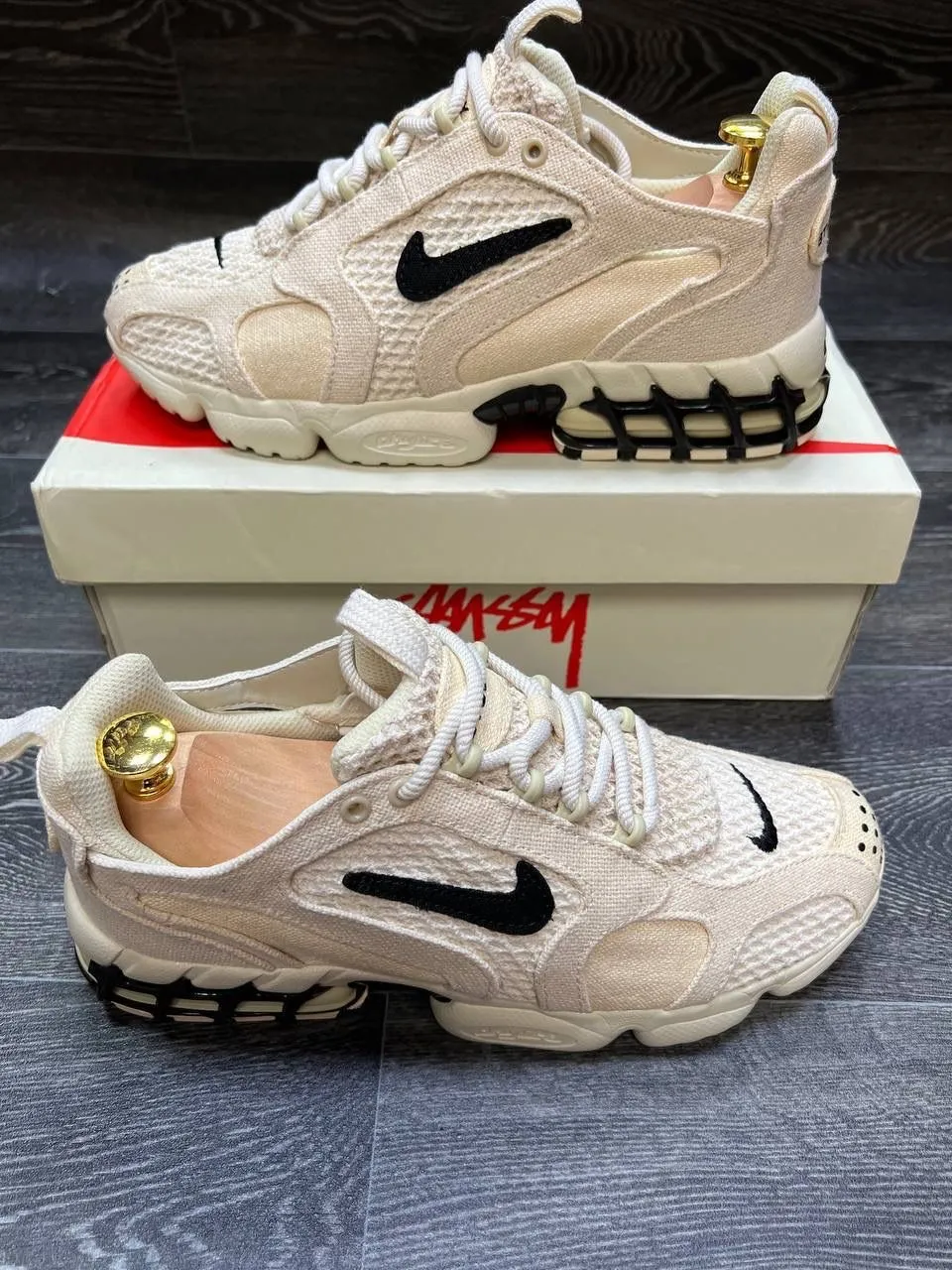 Zapatillas deportivas color crudo con detalles en negro y logo de Nike y Stussy. Cordones blancos.