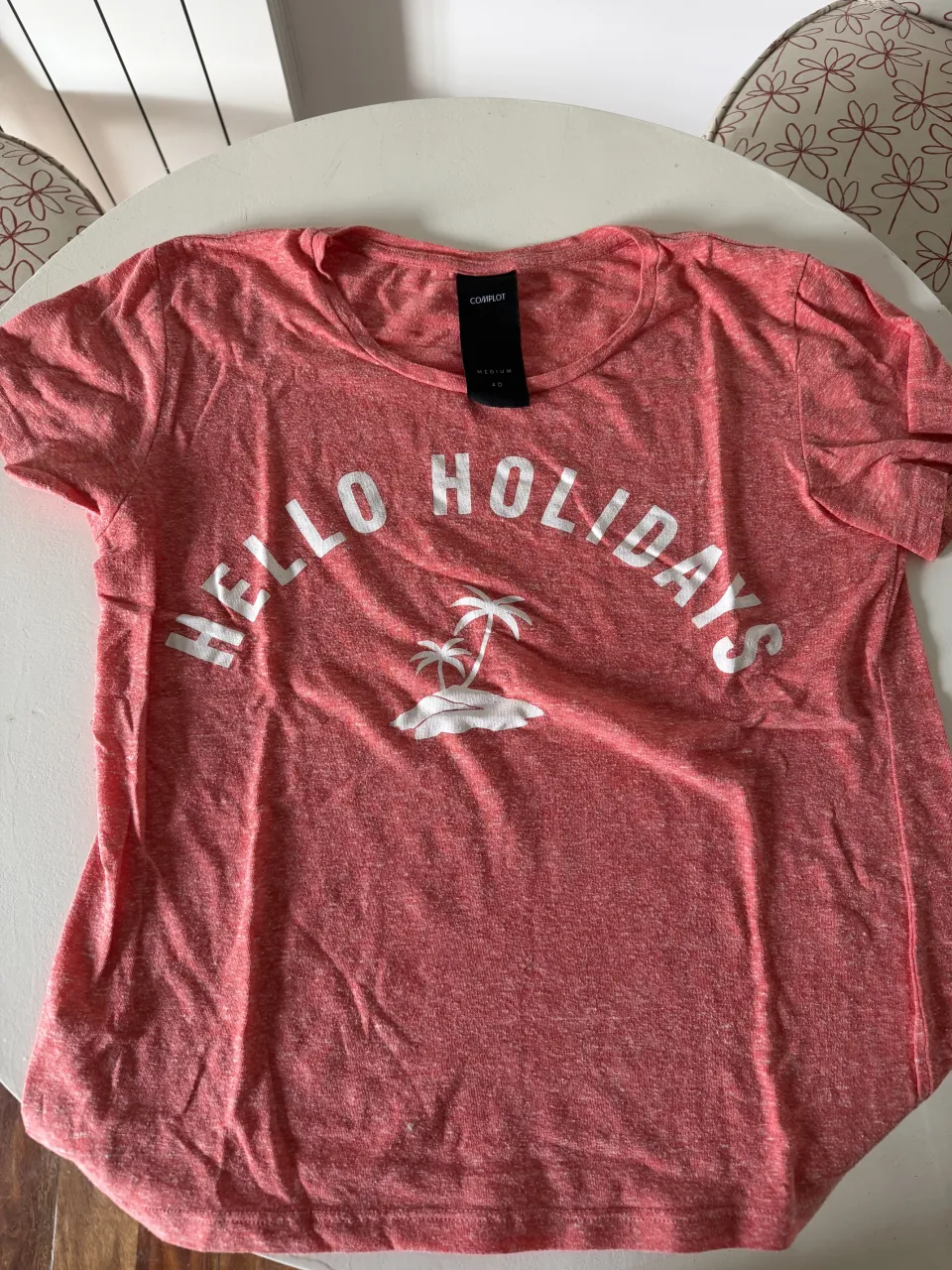 Remera de algodón color salmón con estampa "HELLO HOLIDAYS" y palmeras. Ideal para un look casual y veraniego.