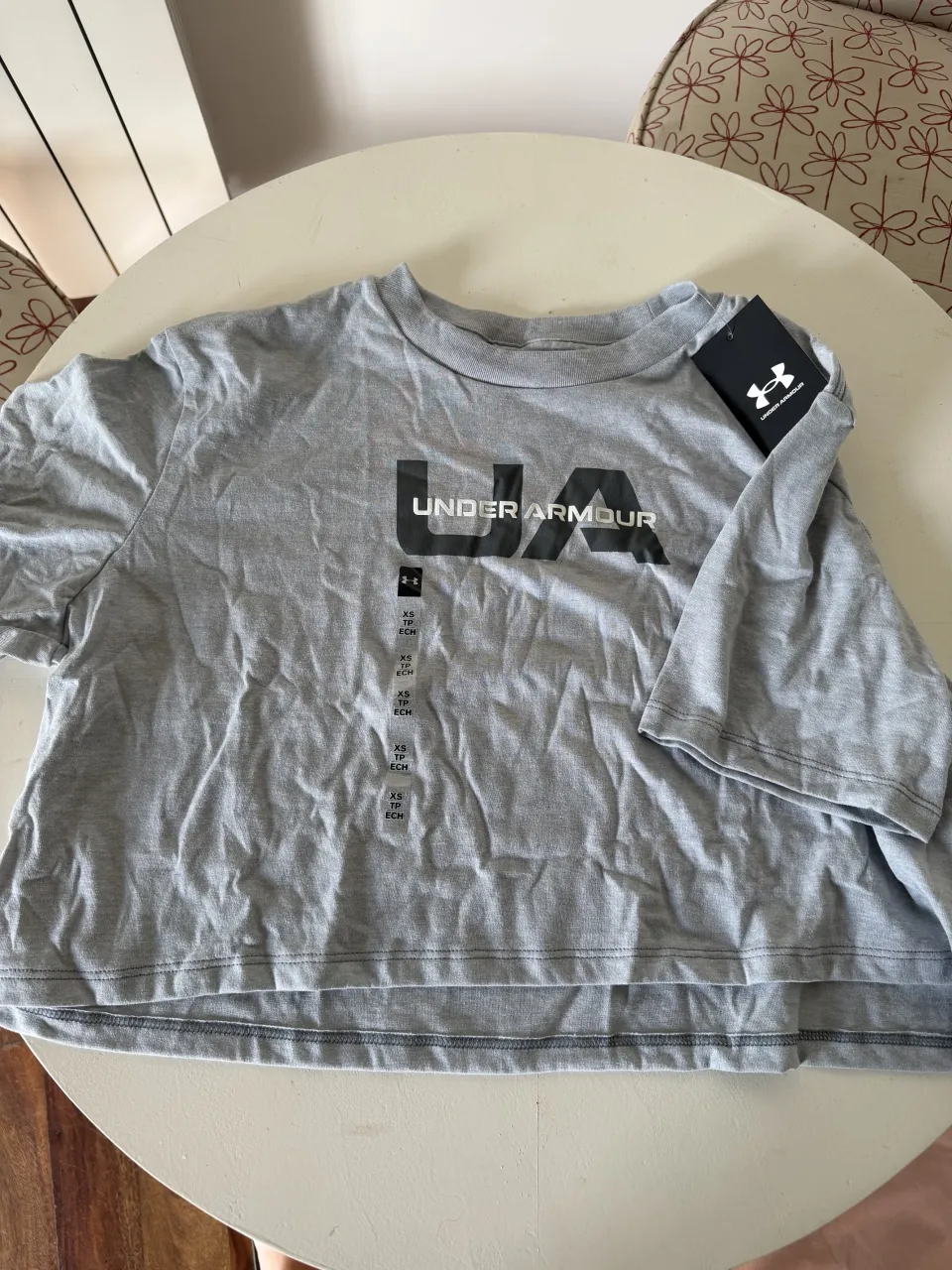 Remera gris de algodón, corta y suelta, con el logo de Under Armour estampado en el frente. Ideal para un look casual y deportivo.