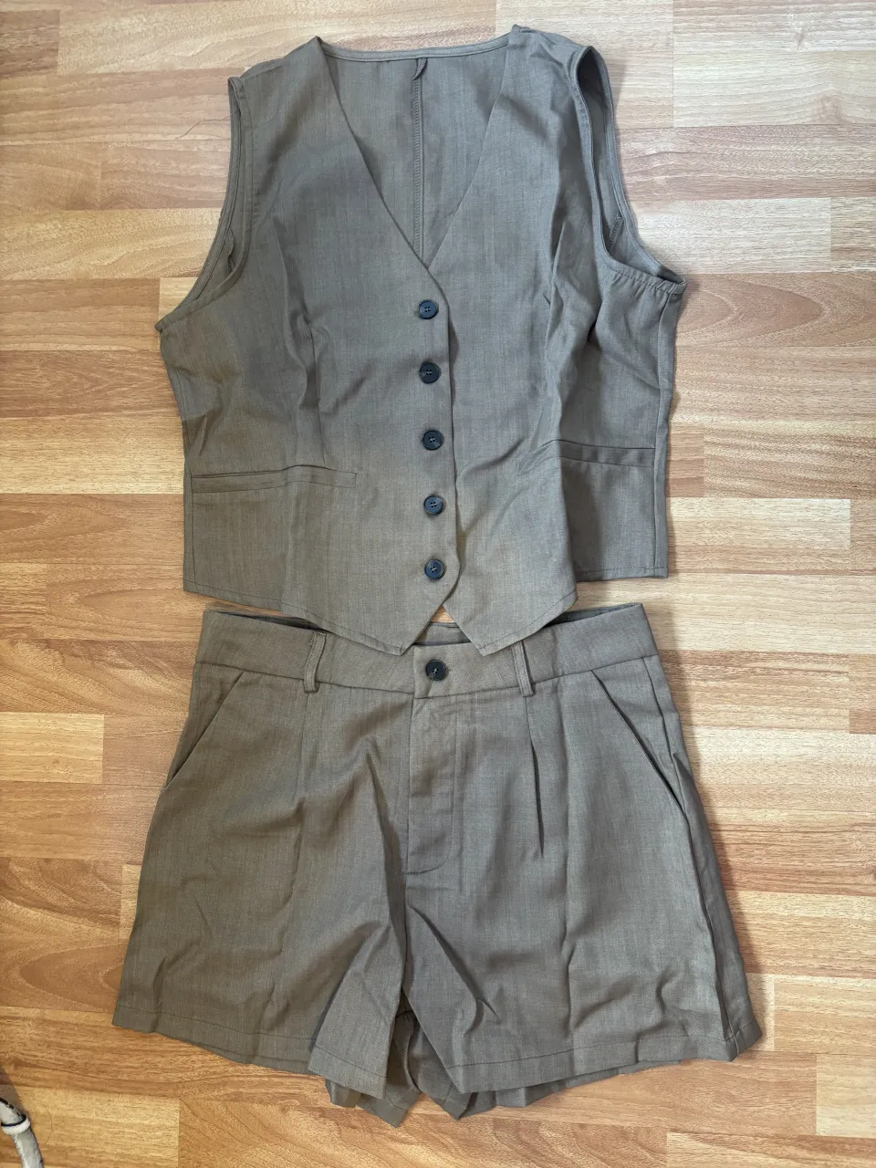 Conjunto de chaleco y shorts de vestir color marrón . El chaleco es sin mangas, con cuello en V y cuatro botones al frente. El short tiene dos bolsillos laterales y un botón al frente.