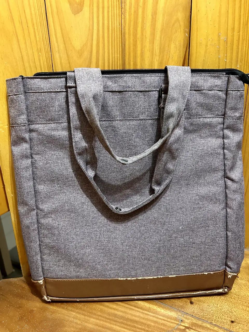 Bolso tote gris con detalles marrones en la base. Ideal para llevar todo lo necesario con estilo y comodidad. Perfecto para el día a día.