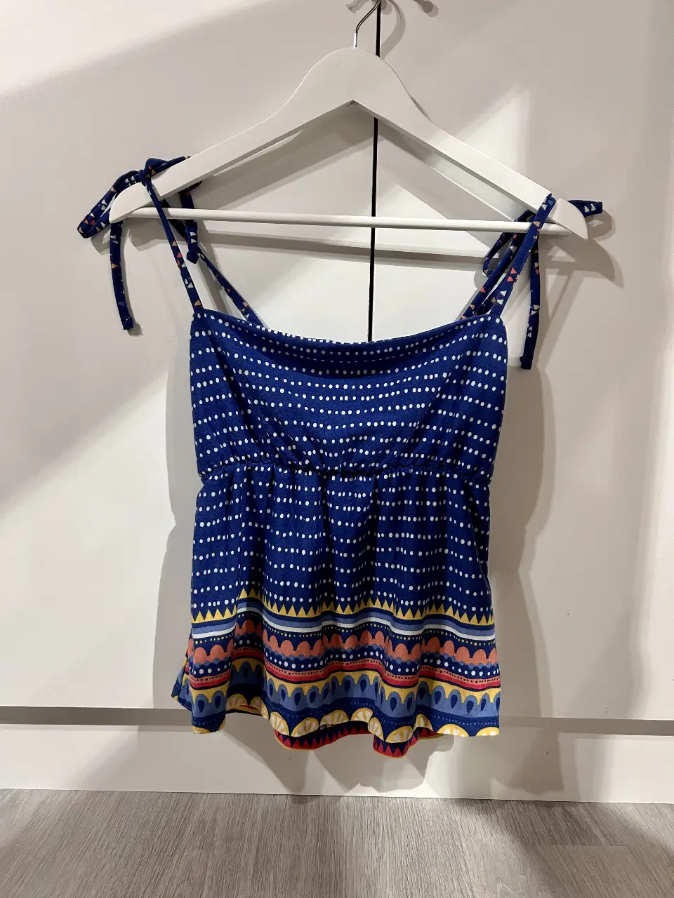 Top de mujer azul con estampado de lunares blancos y detalles geométricos en la parte inferior. Con tirantes ajustables y diseño fresco, ideal para el verano.