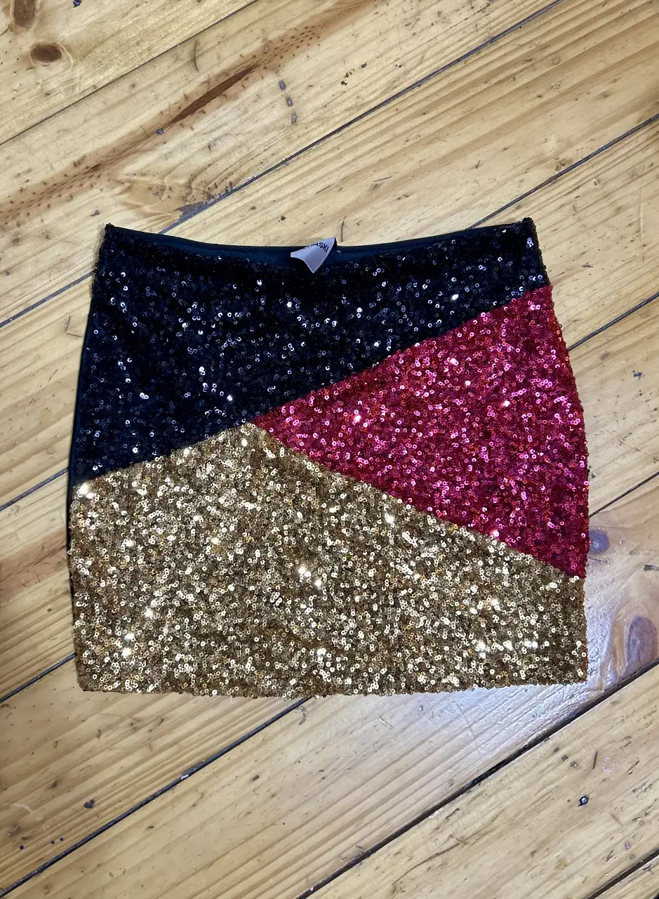 Minifalda de lentejuelas con diseño geométrico en negro, dorado y fucsia. Ideal para fiestas y eventos especiales.