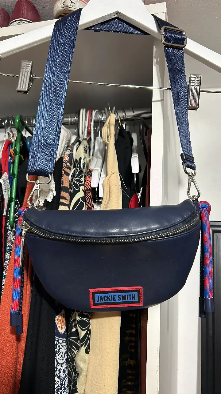 Bandolera Jackie Smith azul marino con correa ajustable. Diseño semicircular con cierre y detalle de borlas en los extremos. Ideal para llevar tus esenciales con estilo.