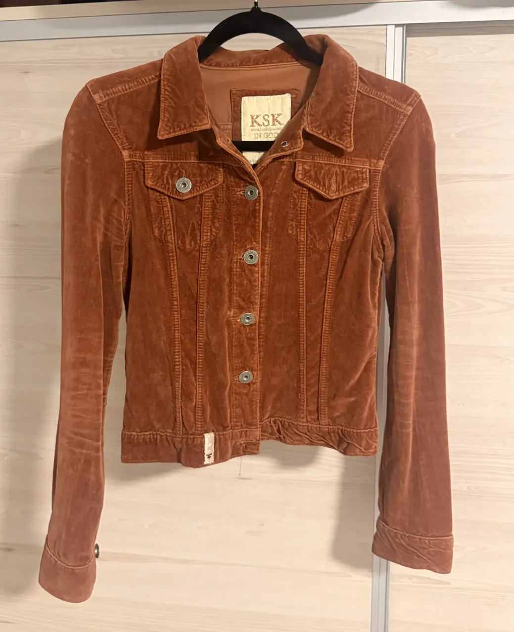 Campera de pana color marrón. Tiene cuello solapa, botones al frente y dos bolsillos con tapa en el pecho. Mangas largas con puños abotonados.