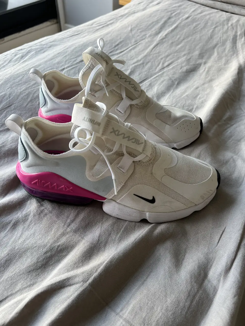 Zapatillas Nike Air Max Infinity 2 para mujer, blancas con detalles en rosa y negro. Talle 9.5 US. Diseño moderno y cómodo, ideales para uso diario y actividades deportivas.