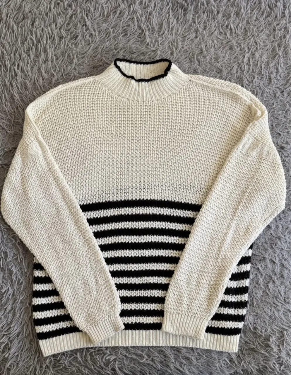 Sweater de tejido de punto con cuello alto y detalles de rayas horizontales en la parte inferior. El cuello y el borde inferior tienen un detalle de ribb negro.