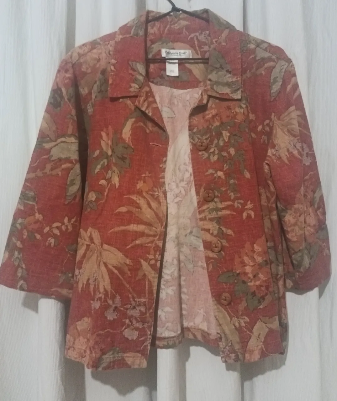 Campera estampada con flores y hojas en tonos rojos, verdes y ocres. Posee cuello solapa, manga 3/4 y cuatro botones de madera al frente.