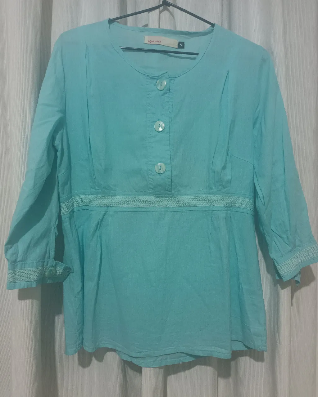 Remera color celeste con mangas 3/4. Posee botones nacarados en la parte superior y detalles de puntilla en puños y cintura. Tela bambula. 