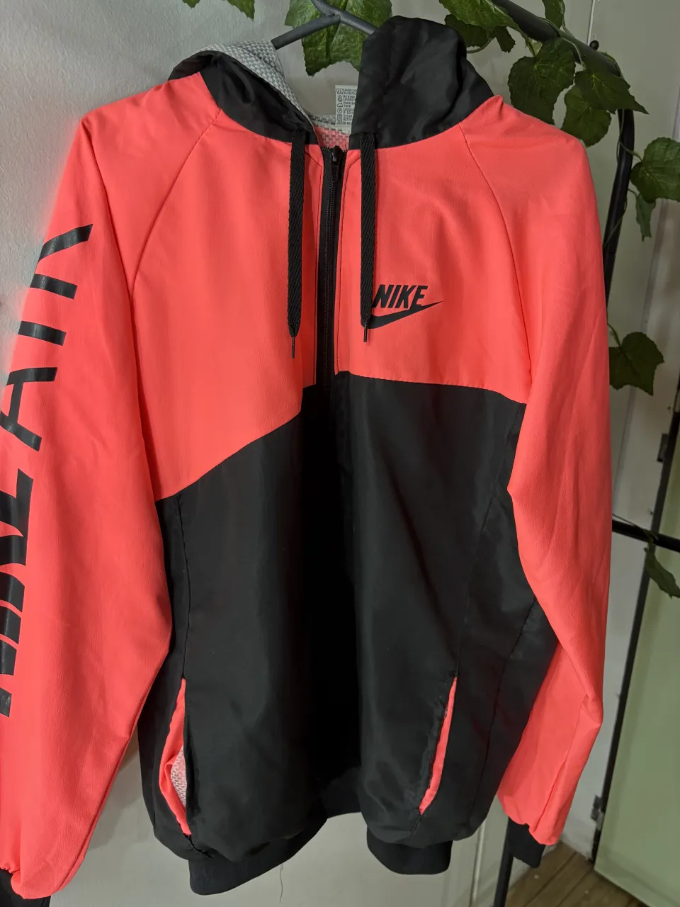 Campera deportiva Nike, ideal para entrenamientos o uso casual. Diseño moderno con bloques de color en coral y negro, y logo de la marca en la manga. Capucha y cierre frontal.