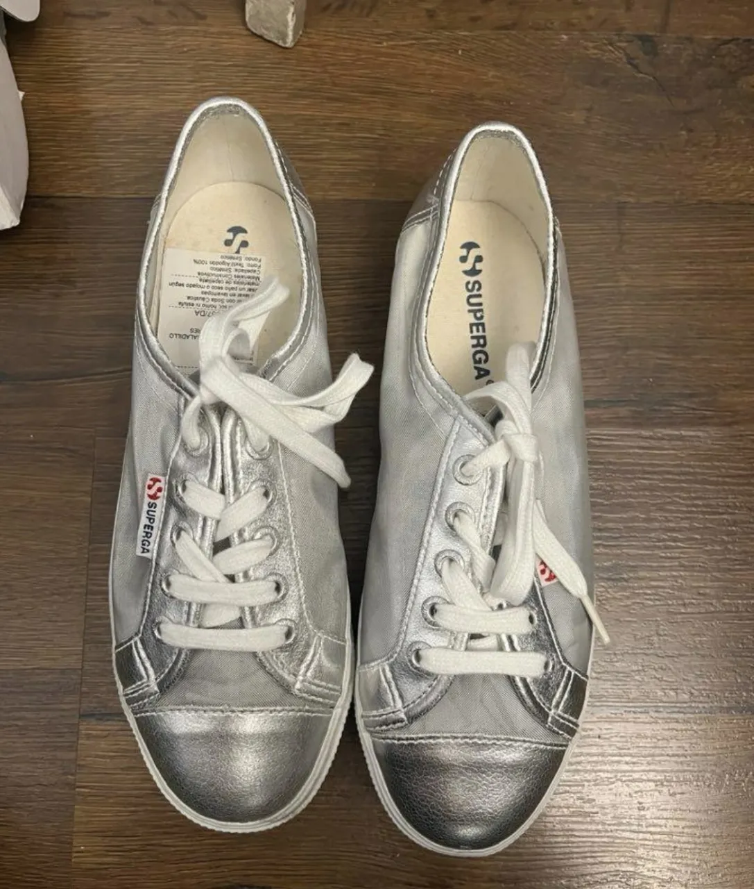 Zapatillas Superga plateadas con cordones blancos y detalles en plateado metalizado. La tela es de red transparente en los laterales.