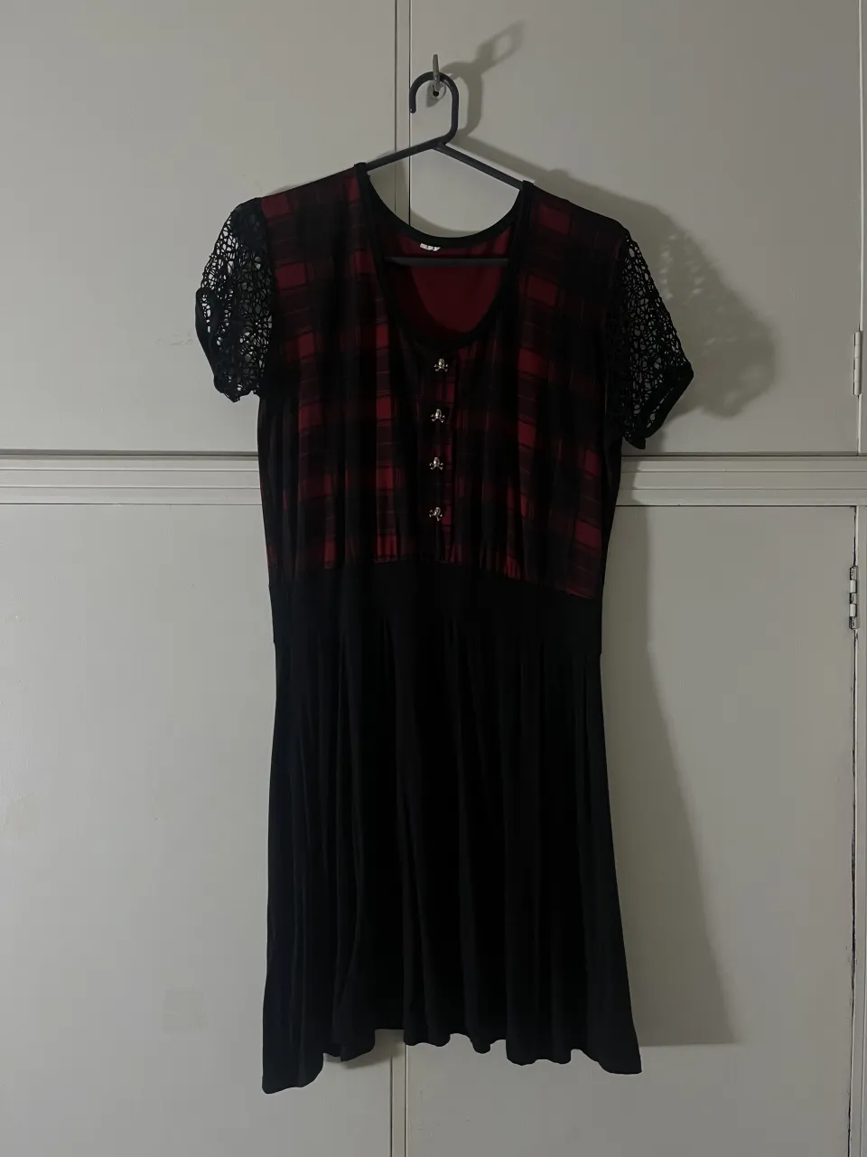 Vestido corto con estampa escocesa en rojo y negro en la parte superior. Las mangas son cortas y de encaje negro. La parte inferior es lisa y negra.