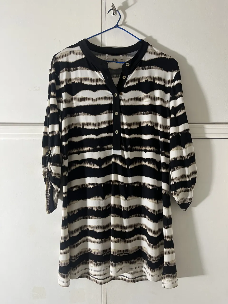 Remera estampada con rayas horizontales en blanco, negro y tonos marrones. Tiene cuello mao con botones y mangas 3/4.