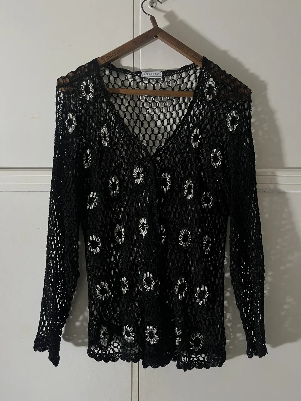 Remera de manga larga de crochet negra con detalles florales blancos bordados. Posee cuello en V y terminaciones de puños y ruedo con guarda tejida.