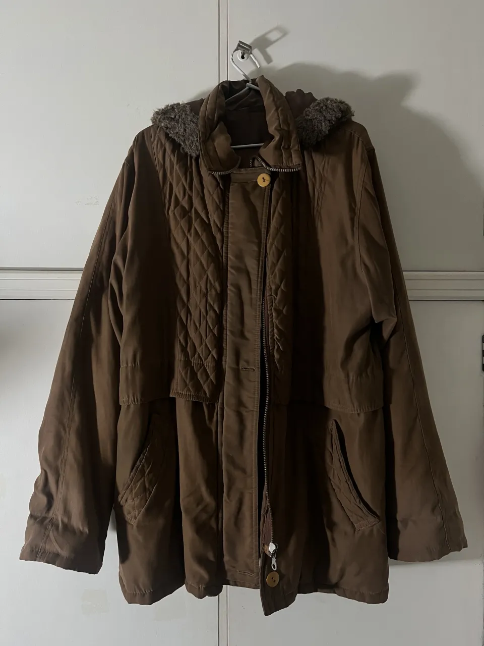 Campera marrón con capucha forrada en peluche. Posee cuello alto, cierre y botones a la vista. Tiene bolsillos frontales y detalles acolchados en rombos en el frente y en los bolsillos.