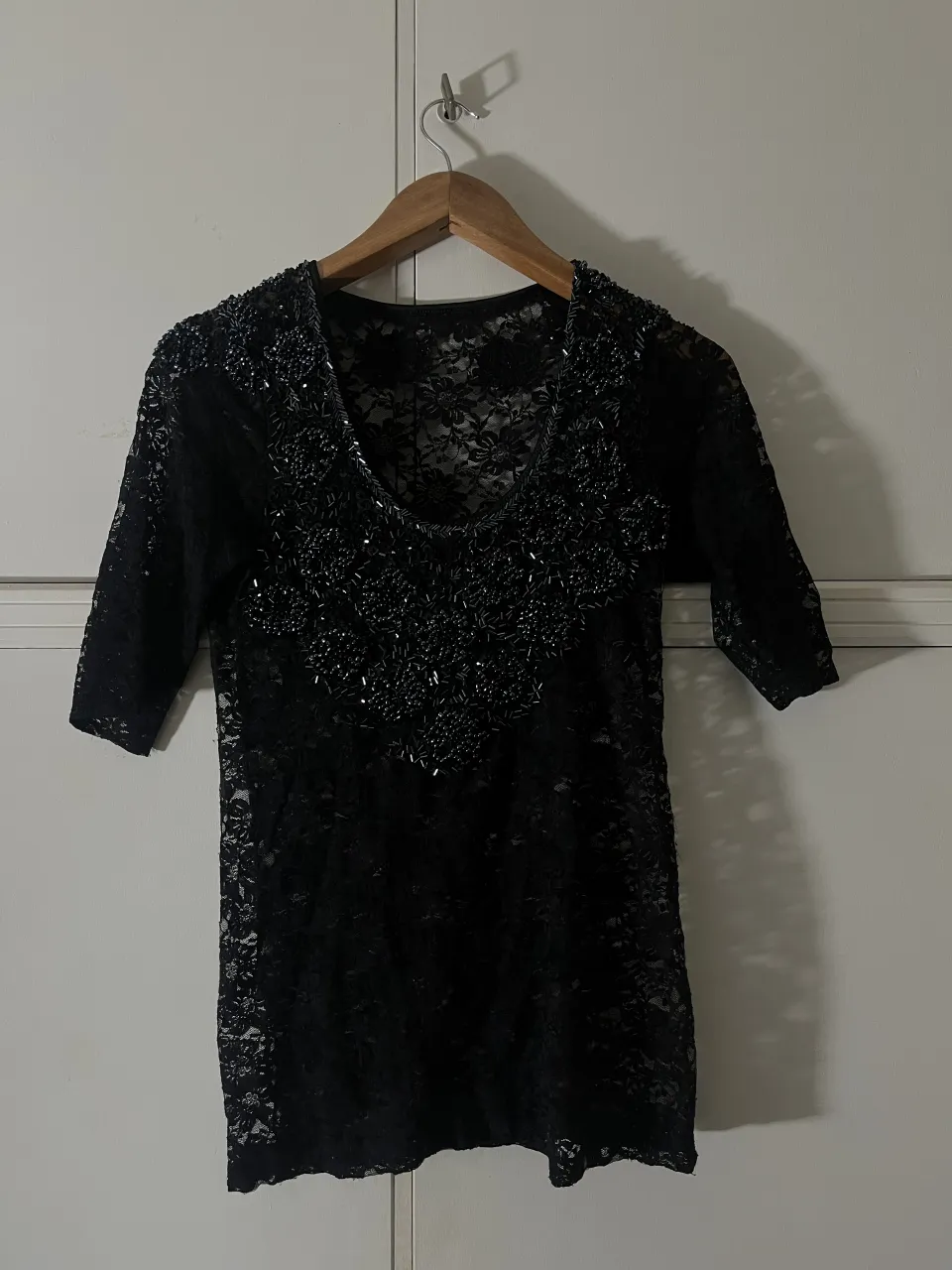 Remera negra de encaje con mangas 3/4. Posee detalles de pedrería y bordados en el escote y la parte superior delantera.