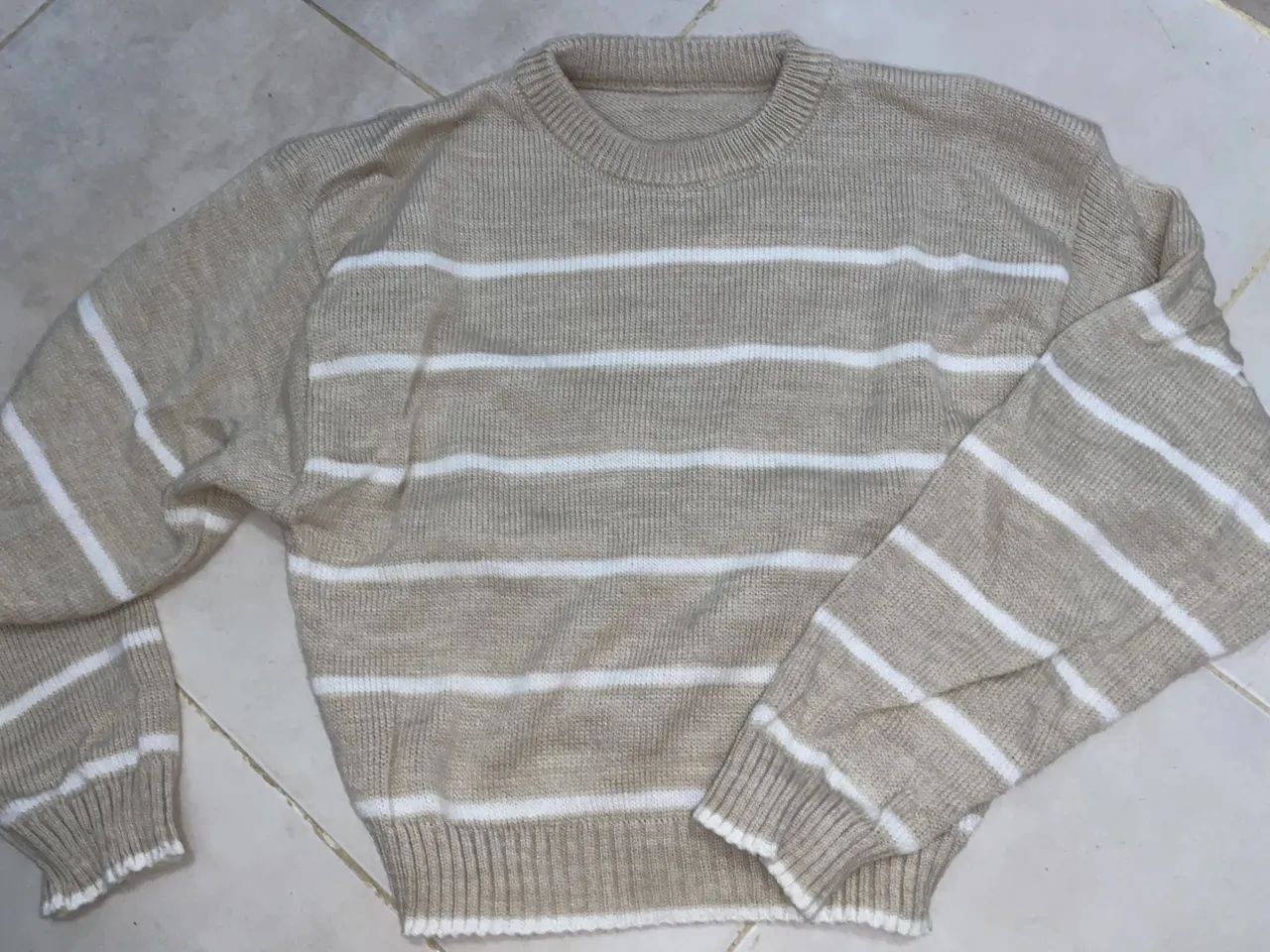 Sweater de tejido de punto con rayas horizontales en color crudo y blanco. Posee cuello redondo y mangas largas.