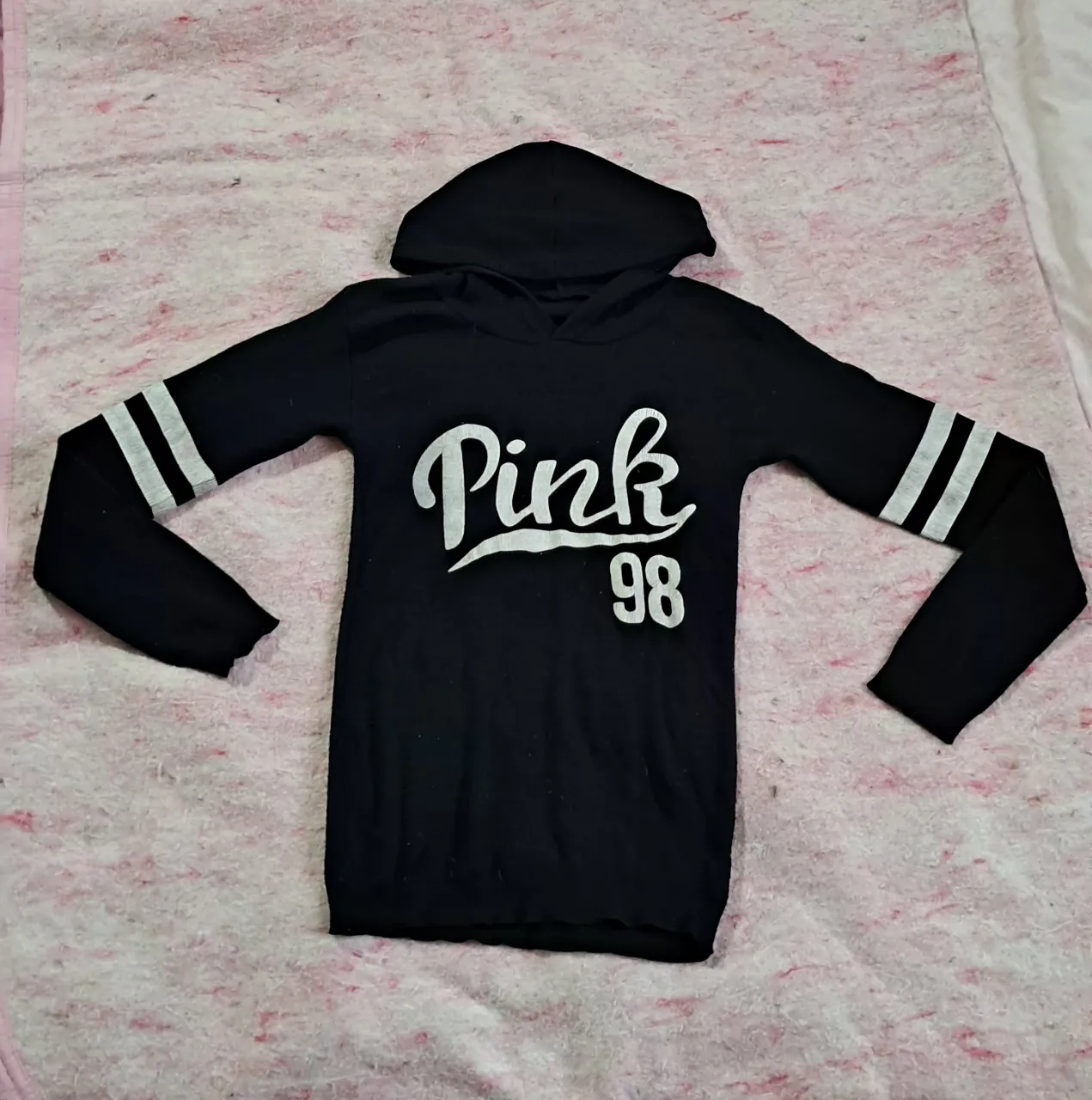 camiseta tipo buzo, negro con capucha y mangas largas. Presenta un estampado blanco con la palabra "Pink" y el número "98". Las mangas tienen dos franjas blancas a la altura del antebrazo.