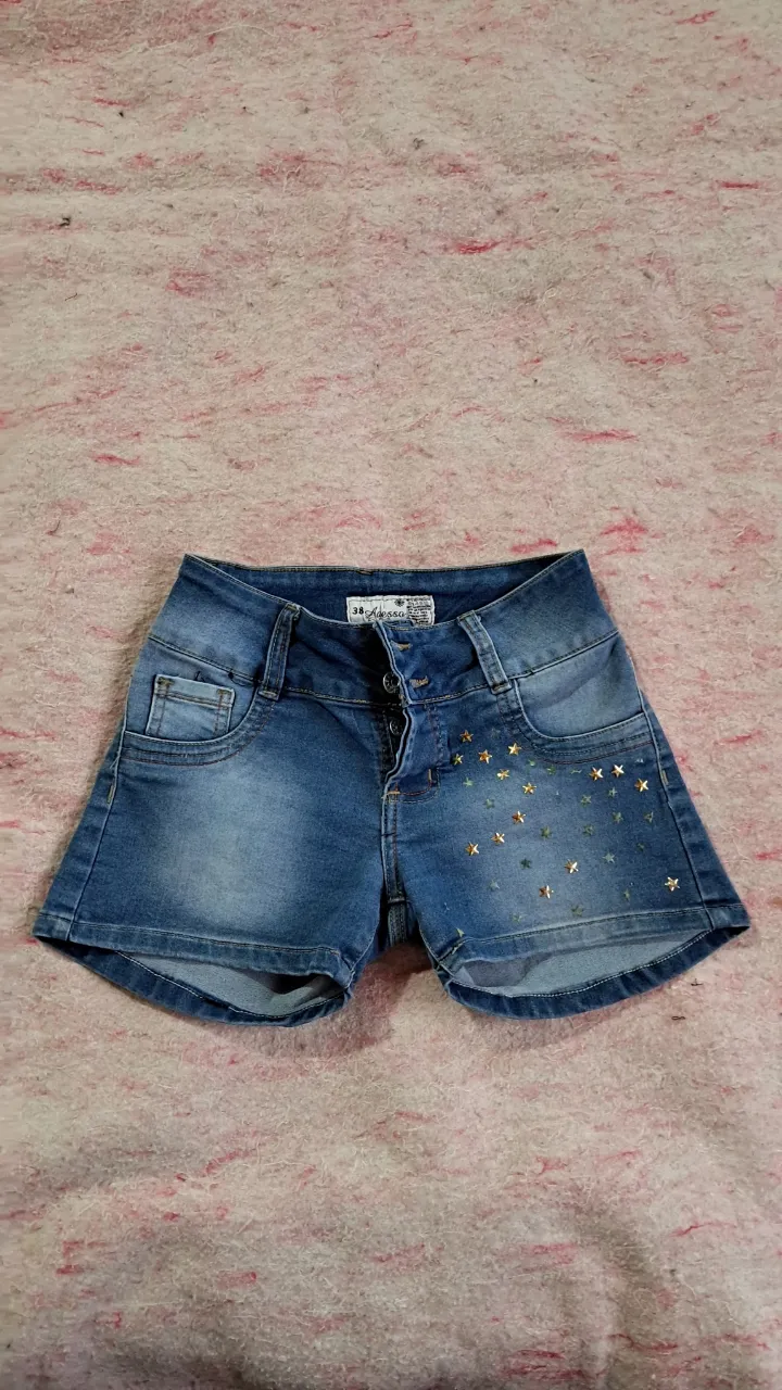 Shorts de jean tiro alto con botones al frente y detalles de estrellas doradas y plateadas en el frente. Bolsillos delanteros y traseros.