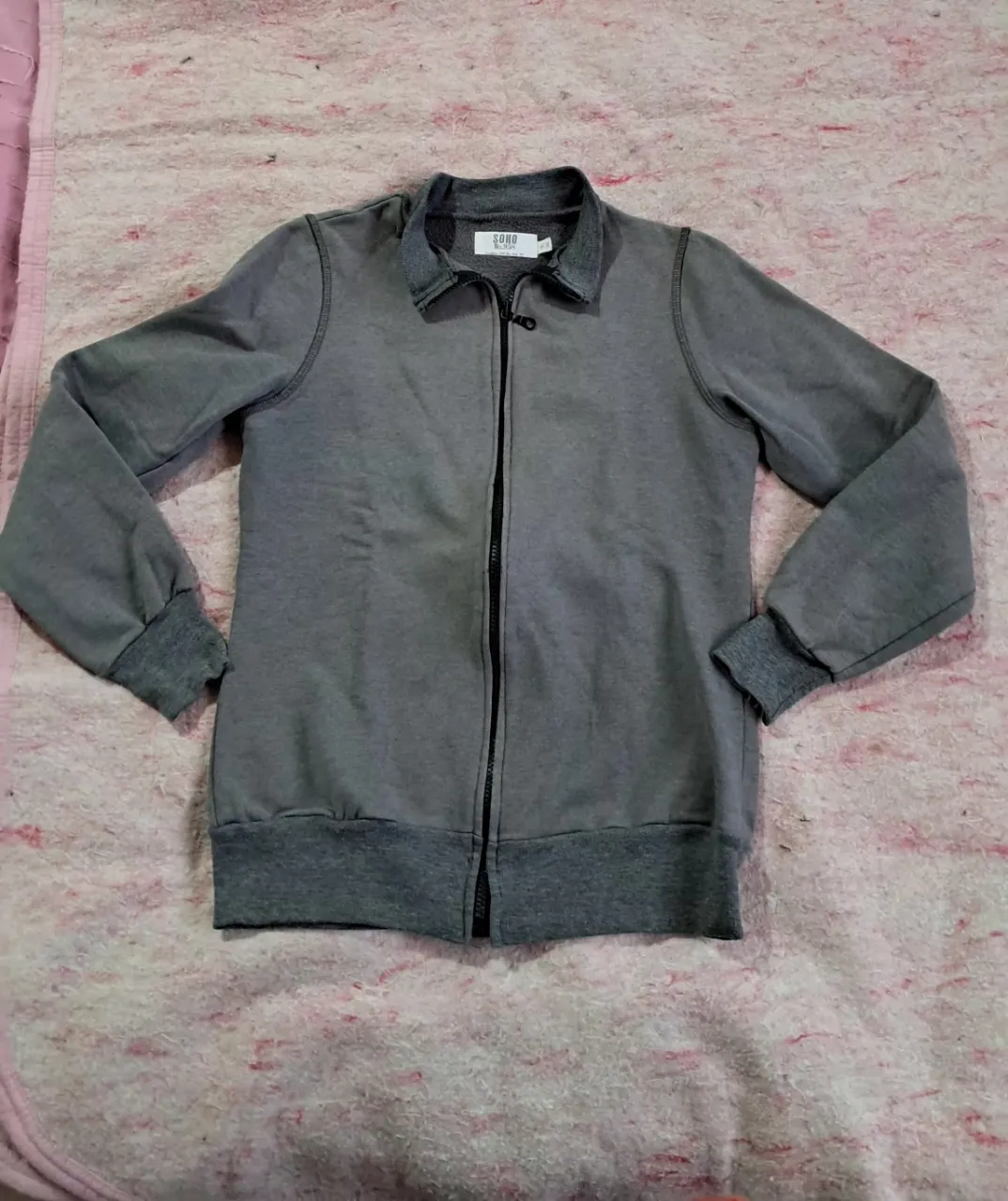 Buzo gris con cierre completo y cuello tipo polo. Puños y cintura elastizados.