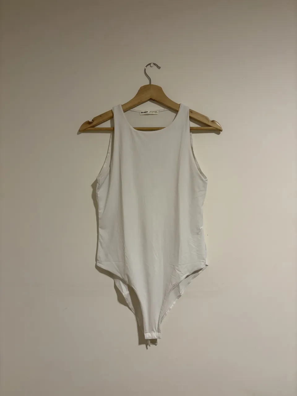 Body blanco sin mangas, con cuello redondo y broche inferior.