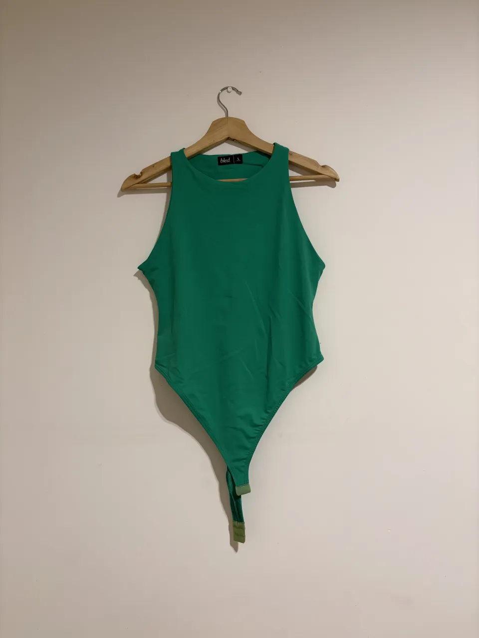 Body de color verde con cuello redondo y sin mangas. Cierre de broche en la parte inferior.