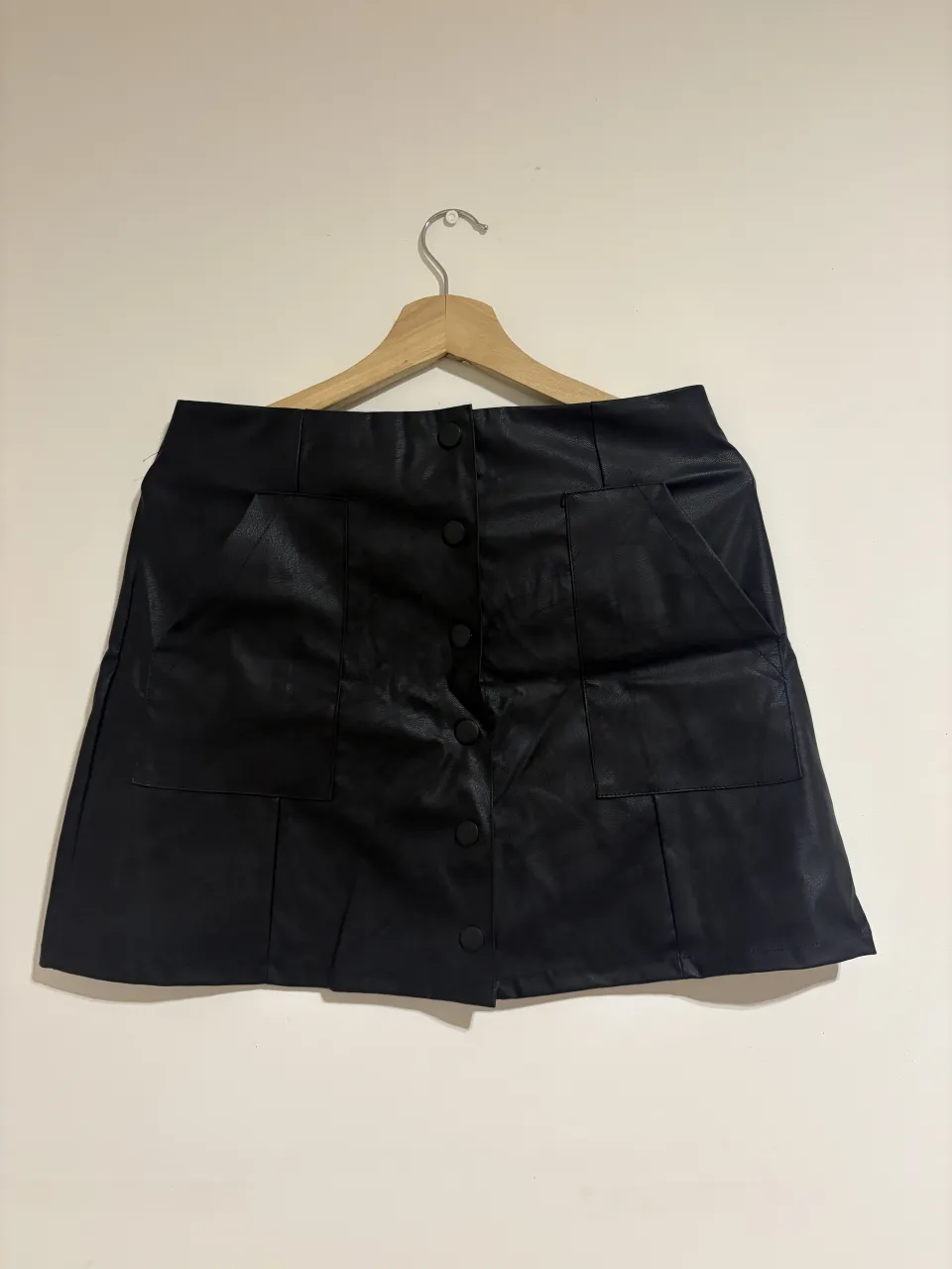 Pollera negra de cuero sintético con botones al frente y bolsillos.